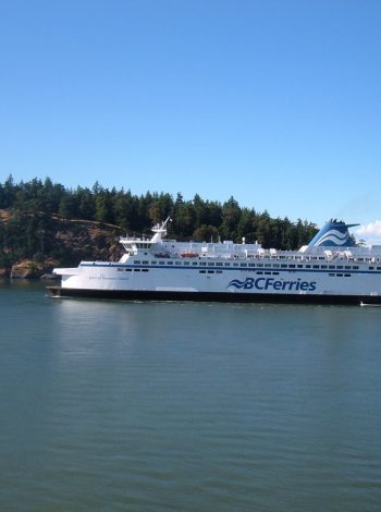 A BC Ferries vessel crossing calm blue water past the forested shoreline of British Columbia's Southern Gulf Islands on the way to Salt Spring Island