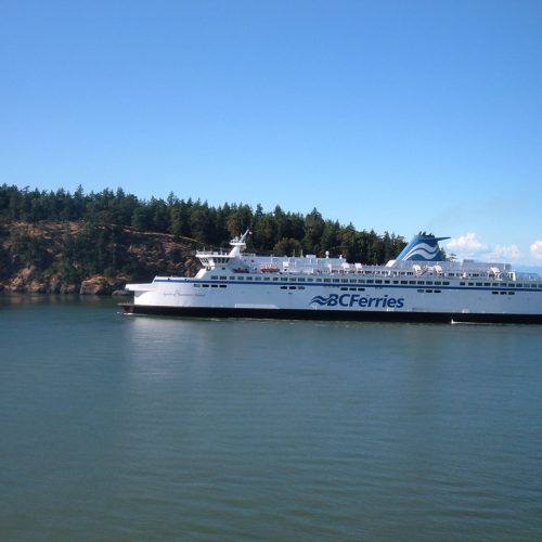 A BC Ferries vessel crossing calm blue water past the forested shoreline of British Columbia's Southern Gulf Islands on the way to Salt Spring Island